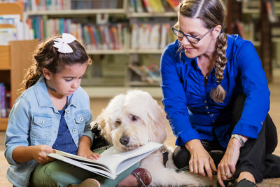 little girl reading a book with a dog and an adult woman